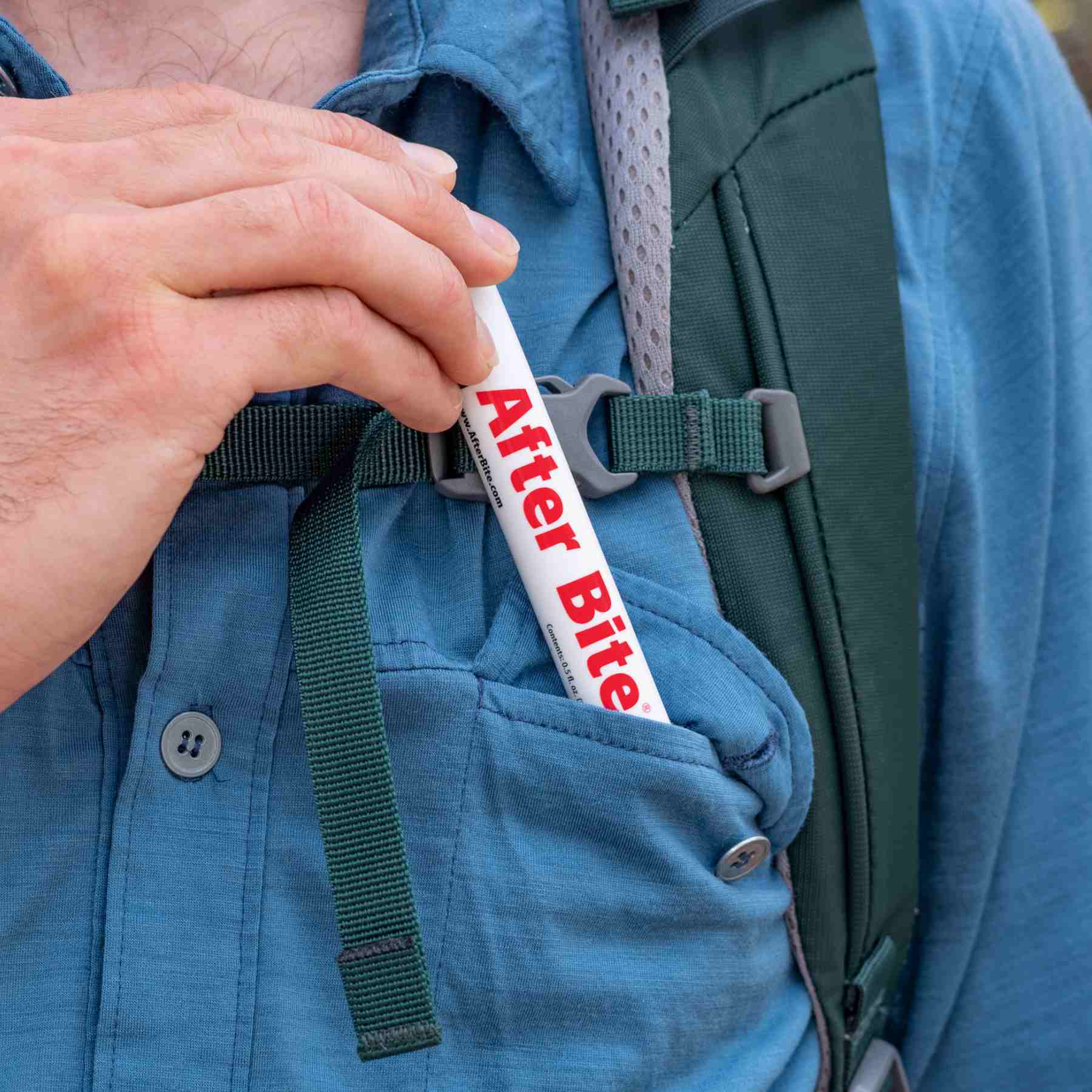 Person in blue button up shirt with green backpack pulling tube of After Bite out of shirt pocket