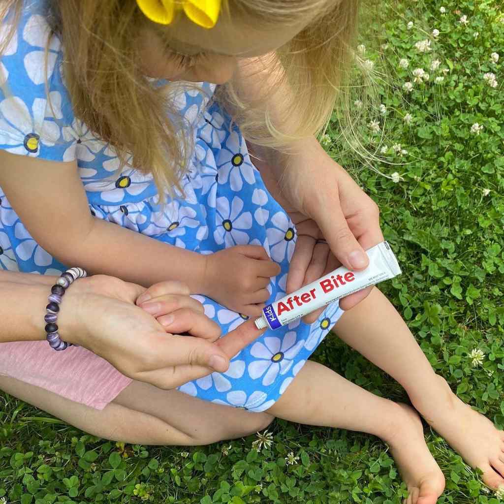 After Bite Kids woman squeezing tube onto finger while sitting behind girl