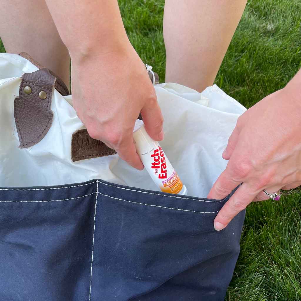 The Itch Eraser Spray pulling from blue and white tote bag in grass