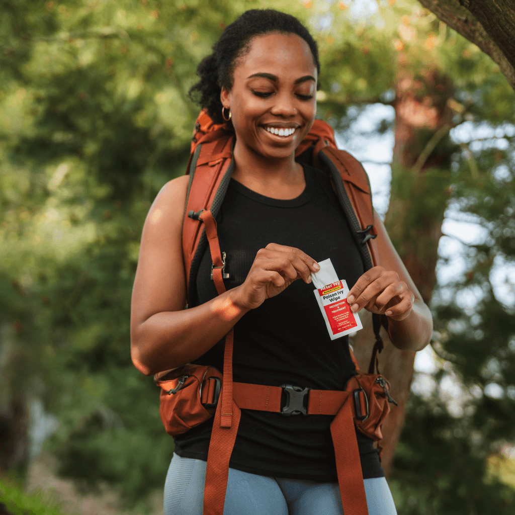 Woman wearing an orange backpack removing After Ivy wipe from packet