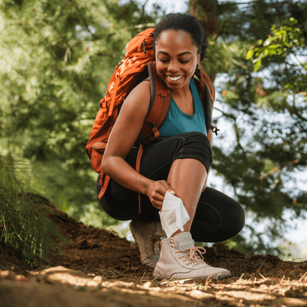Woman using an After Ivy wipe on her leg while on the hiking trail